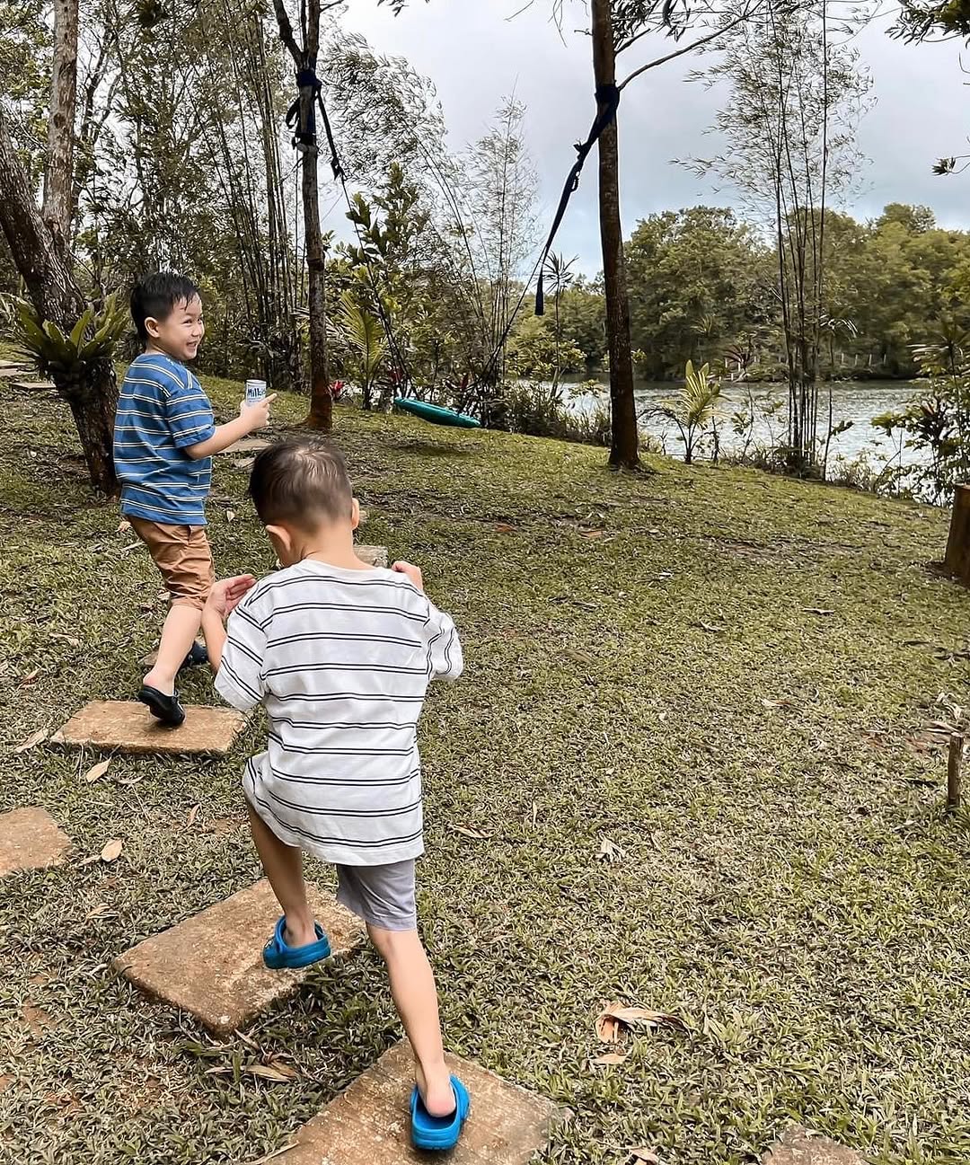 Two young boys playing on stepping stones near the lake shore, surrounded by trees