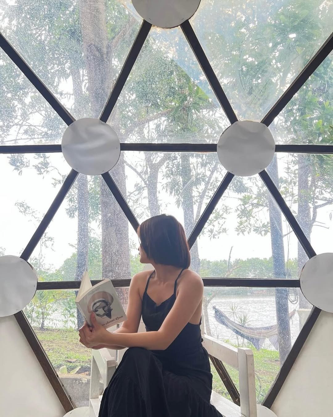 Guest reading a book inside a geodesic dome, lake visible through transparent panels