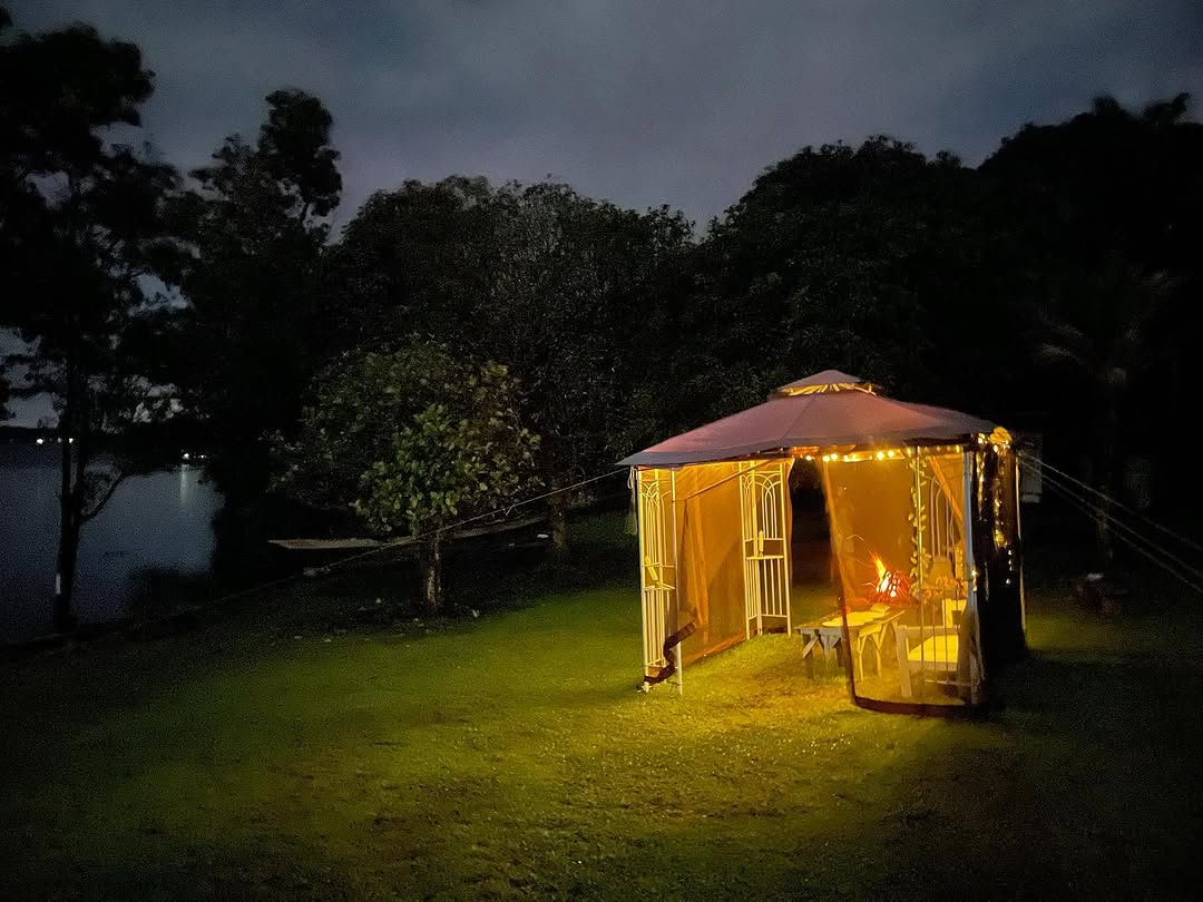 White gazebo illuminated with warm fairy lights at night, lake faintly visible behind