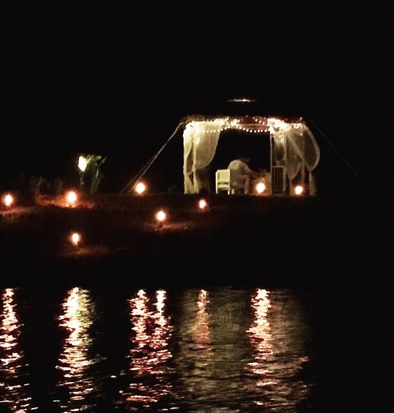 Tent lit by fairy lights and candles at night, warm glow reflected on the dark lake