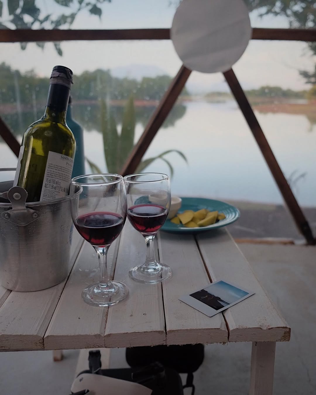 Two wine glasses and bottle on a dome table with lakeside sunset glow through the panels